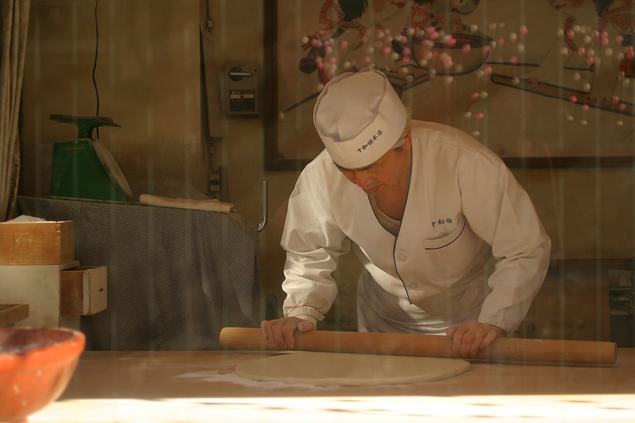 東京・浅草で、木の板の上で手打ちの蕎麦生地を延ばすところ