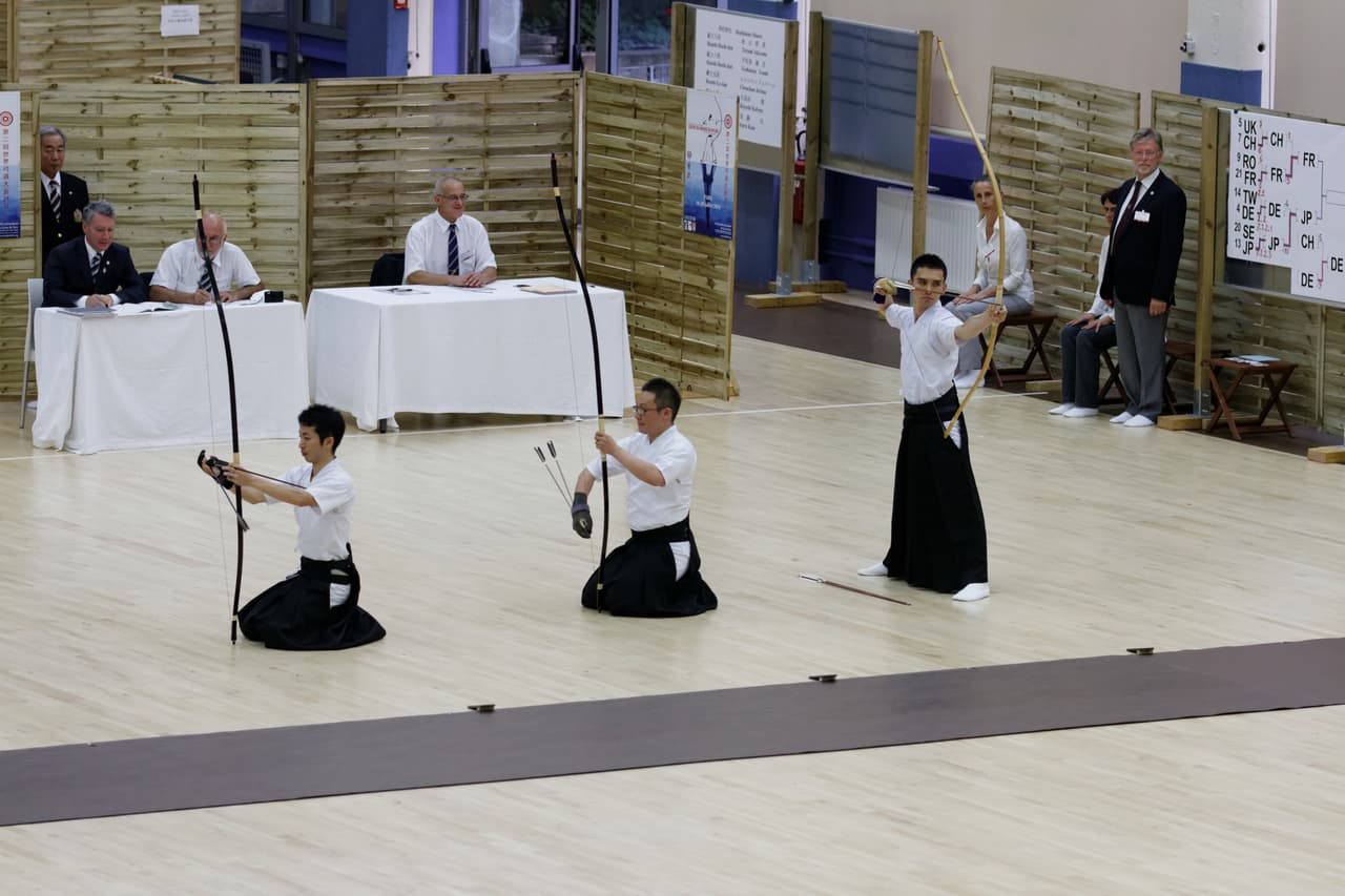 Kyudo archers in white keikogi and black hakama standing in line at the shooting position