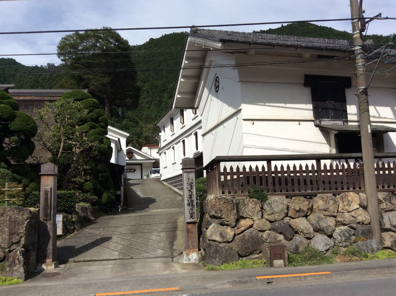 The white-plastered storehouses of Ozawa Shuzo (Sawanoi) on the road through Sawai, Ome, in western Tokyo, with forested hills rising behind