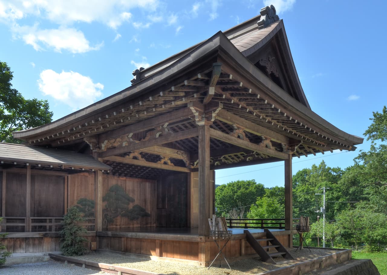 A roofed noh stage with a bridgeway, projecting into the audience