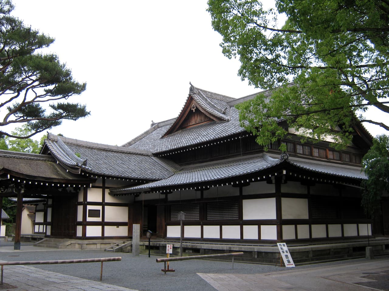 The former Butokuden martial-arts hall in Okazaki, Sakyo-ku, Kyoto — a wooden hall with layered tiled roofs, framed by a pine and a maple
